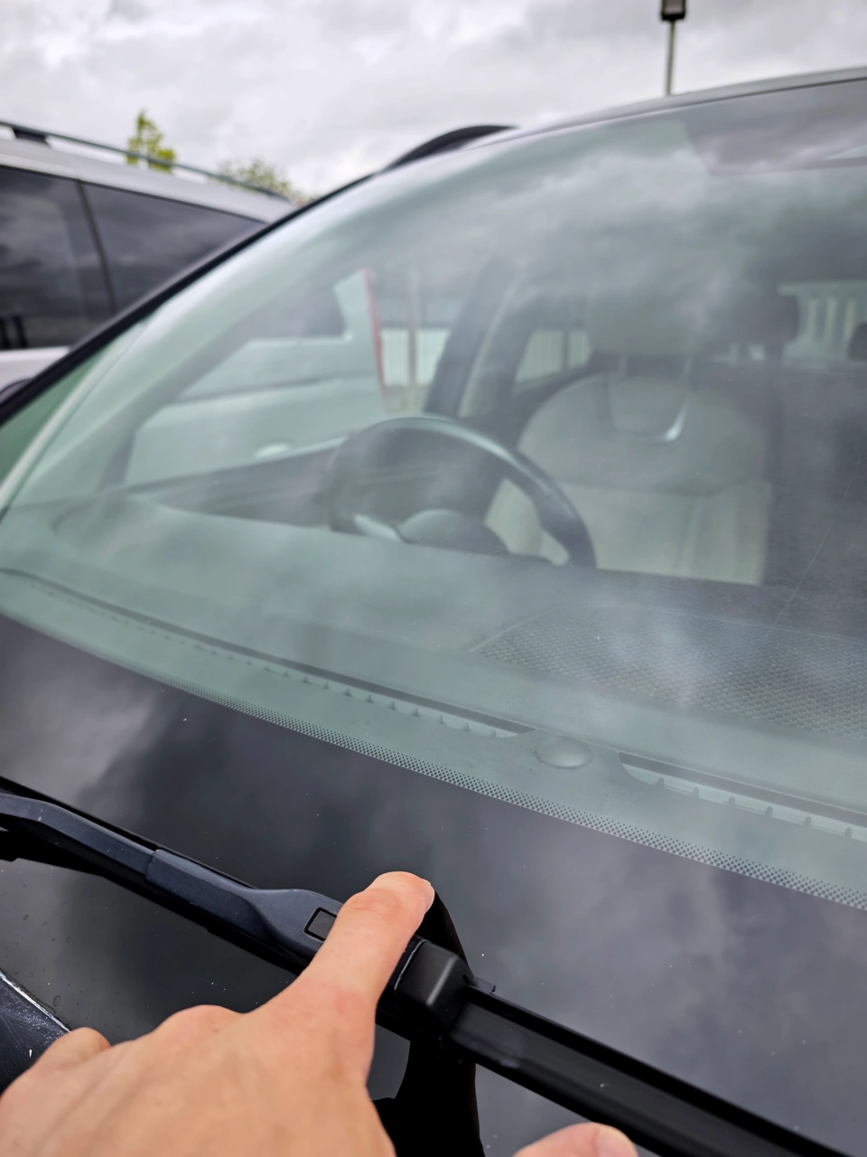 Car windscreen after restoration, photographed from a different angle with a finger pointing near the lower edge.
