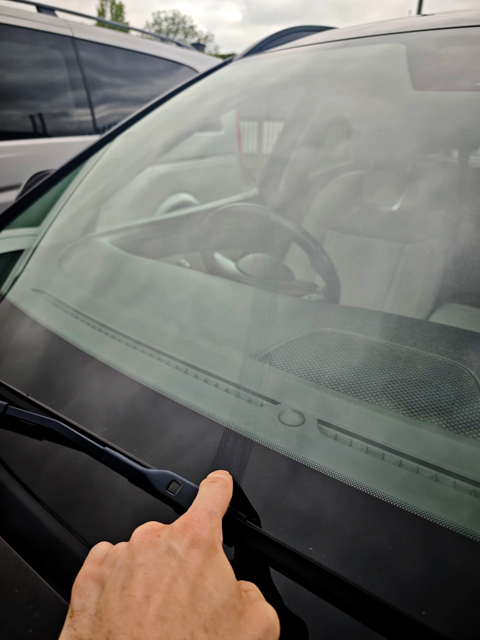 Car windscreen before restoration, with a finger pointing to marks near the lower edge.